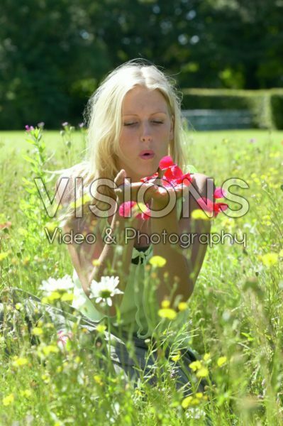 Woman in meadow blowing flower petals